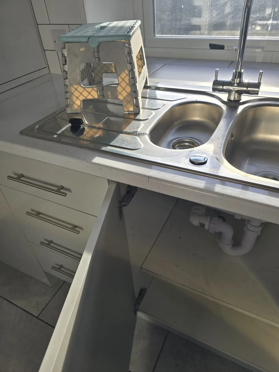 Main Street kitchen sink area after clearance and cleaning work, with the sink cupboard open